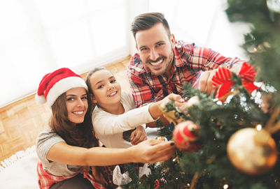 A family of three dressed in holiday clothing putting ornaments on a Christmas Tree