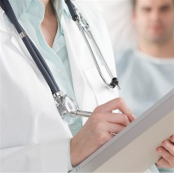 A doctor with a stethoscope around their neck standing beside a patient and writing on a clipboard